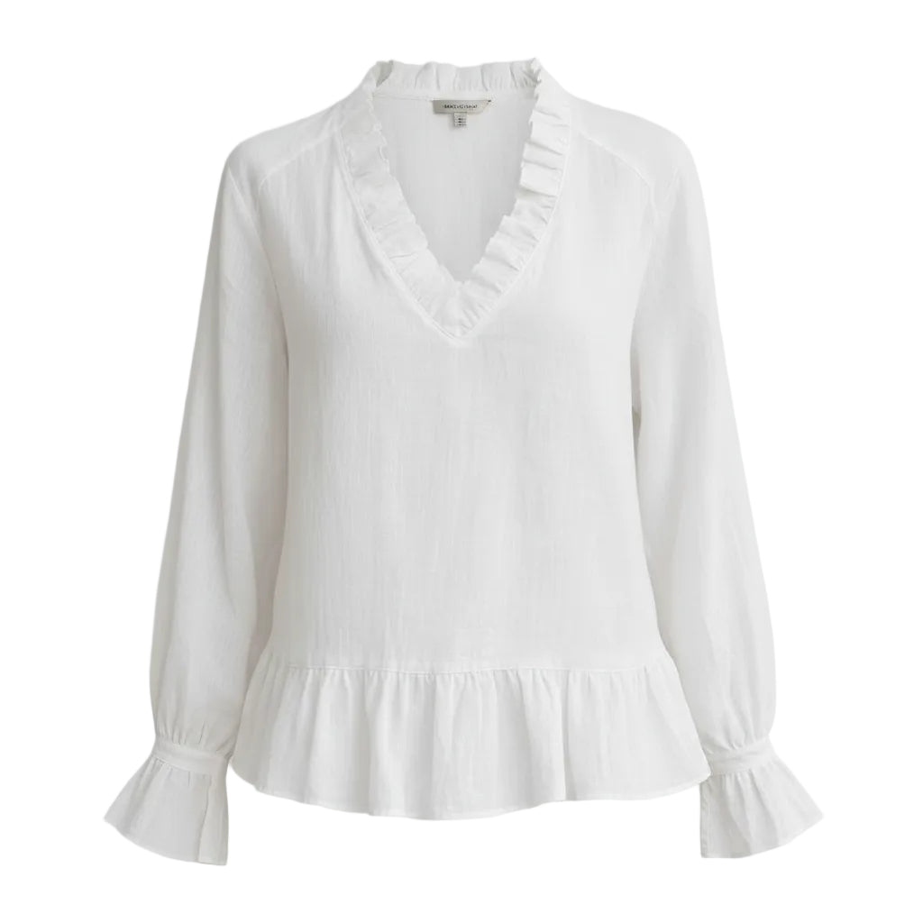 A woman wearing a white long-sleeve blouse with a ruffled V-neckline and ruffled cuffs, paired with white pants, against a plain gray background.