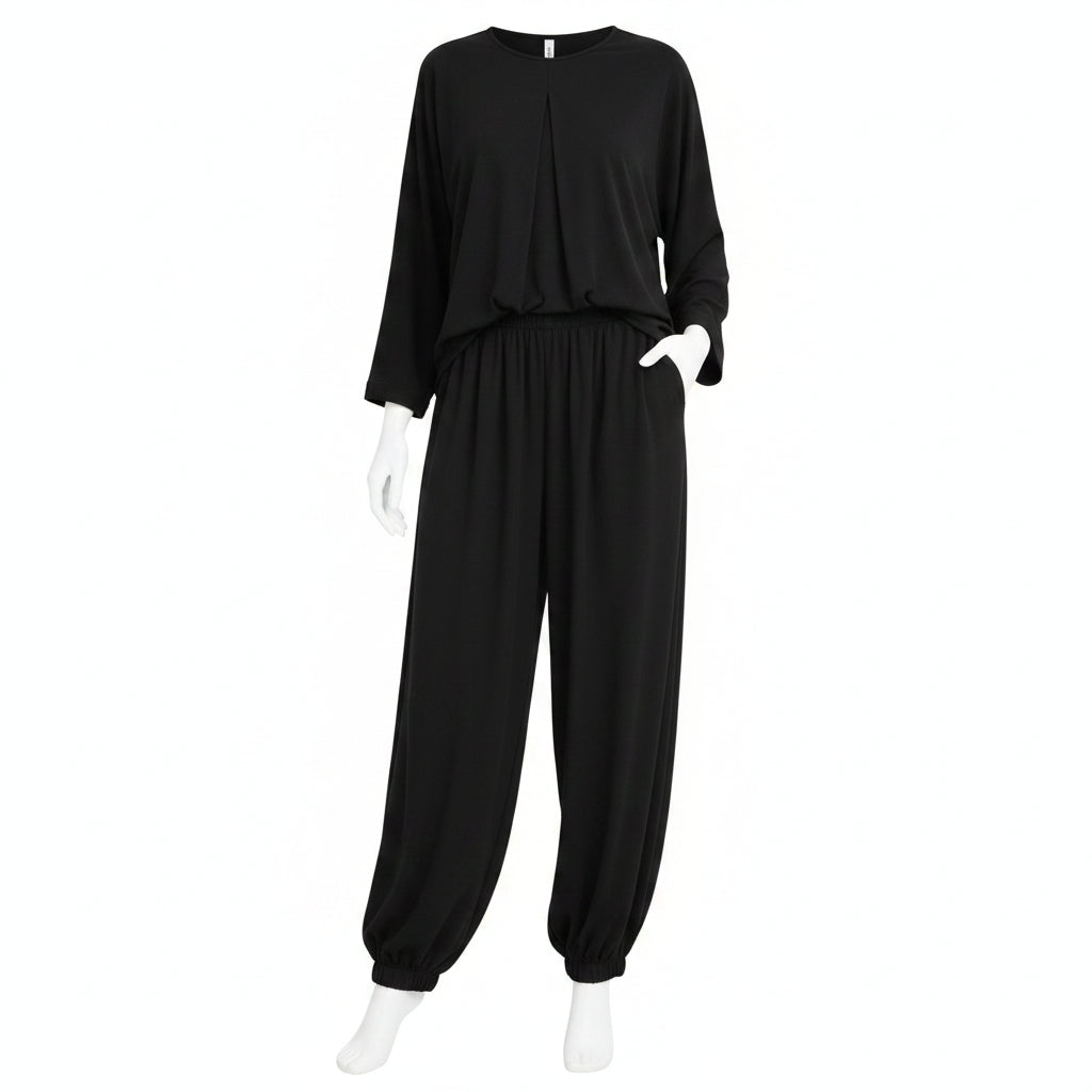 A woman modeling a black two-piece lounge set consisting of a long-sleeve top and matching wide-leg pants, styled with a white handbag, sunglasses, and black sandals in front of a white closet background.