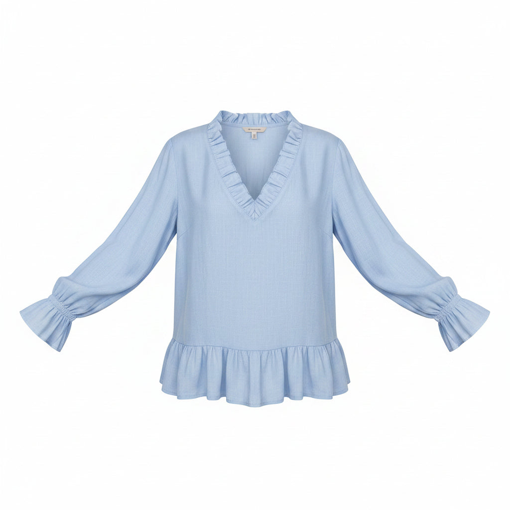 A woman wearing a light blue long-sleeve blouse with a ruffled V-neckline, ruffled cuffs, and a ruffled hem, paired with cream pants against a neutral gray background.