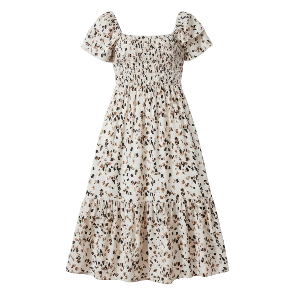 A woman wearing a beige midi dress with a black and brown leopard print pattern, featuring a smocked bodice and short puff sleeves, standing against a white textured wall.