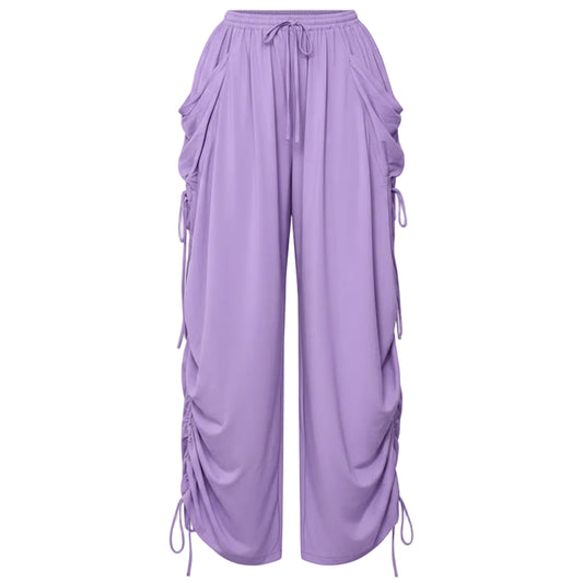 A person wearing loose lavender drawstring pants with side pockets and ruched details down the legs, holding a small black handbag. The photo is cropped from the waist down on a light gray floor against a white wall, with text in the top right reading 'Drawstring Plus Size'.