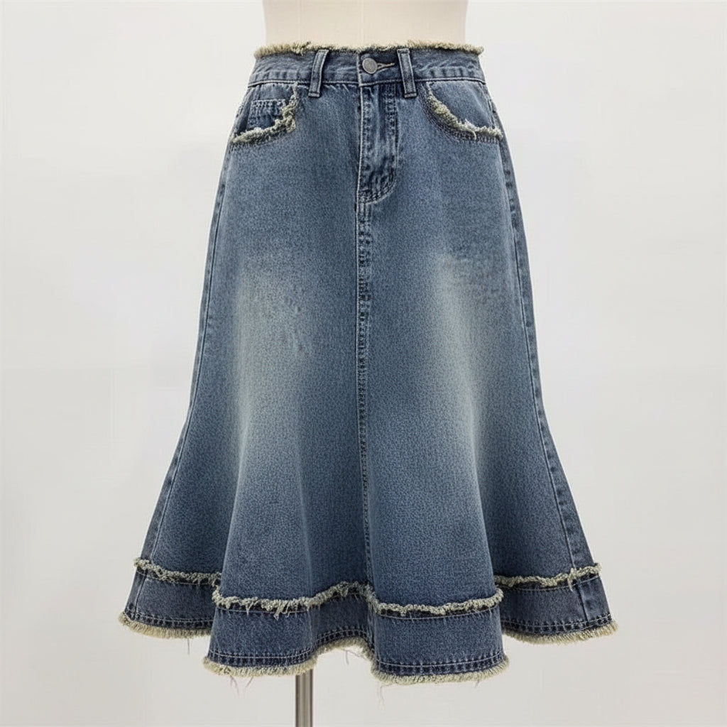 A light blue denim skirt with a high-waisted fit, frayed details on the pockets and hem, and a flared silhouette, shown hanging on a hanger with a hand holding the bottom hem.