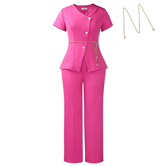 A bright pink two-piece pantsuit featuring a short-sleeve peplum-style top with decorative buttons and a matching waist tie, paired with straight-leg trousers. A gold chain necklace is shown separately to the right on a plain white background.