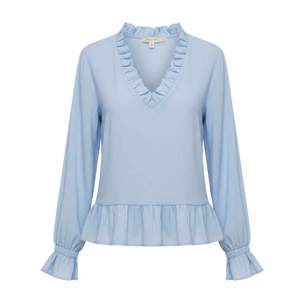 A woman wearing a light blue long-sleeve blouse with a ruffled V-neckline, ruffled cuffs, and a ruffled hem, paired with cream pants against a neutral gray background.