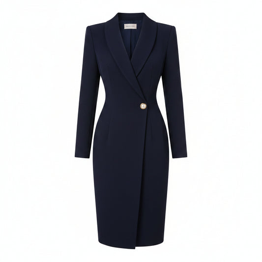 A woman models a navy blue knee-length blazer dress with a shawl collar, single front button, and structured shoulders, holding a white clutch against a light beige wall background.