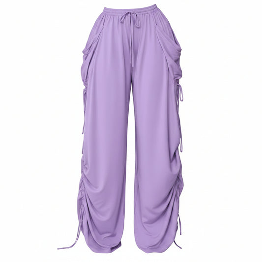 A person wearing loose, wide-leg lavender pants with drawstrings, side pockets, and ruched detailing down the legs, holding a small black handbag. The photo is cropped from the waist down against a plain indoor wall and floor, with text in the top right reading 'Drawstring Plus Size'.